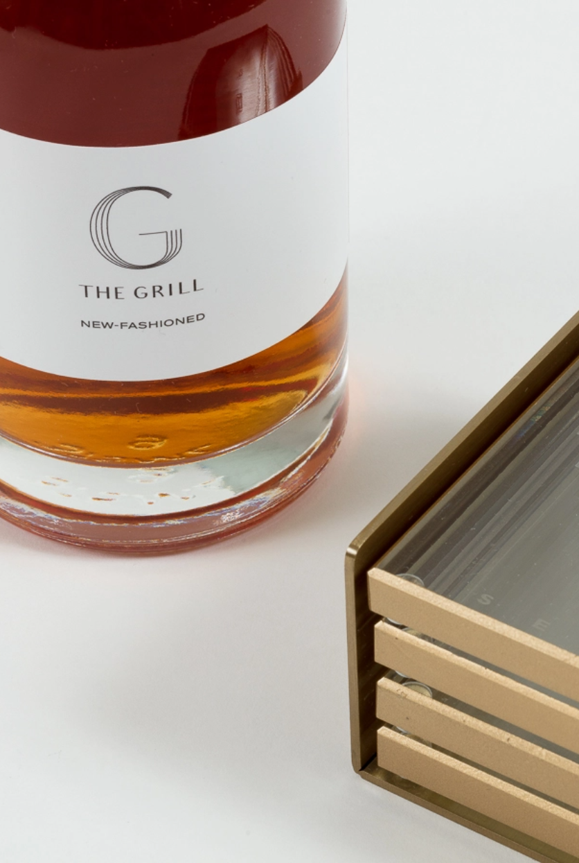 A bottle of the Grill New Fashioned next to coasters